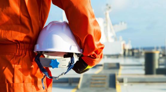 Picture of a person wearing a safety suit and holding a helmet in their hands while standing on a dock.